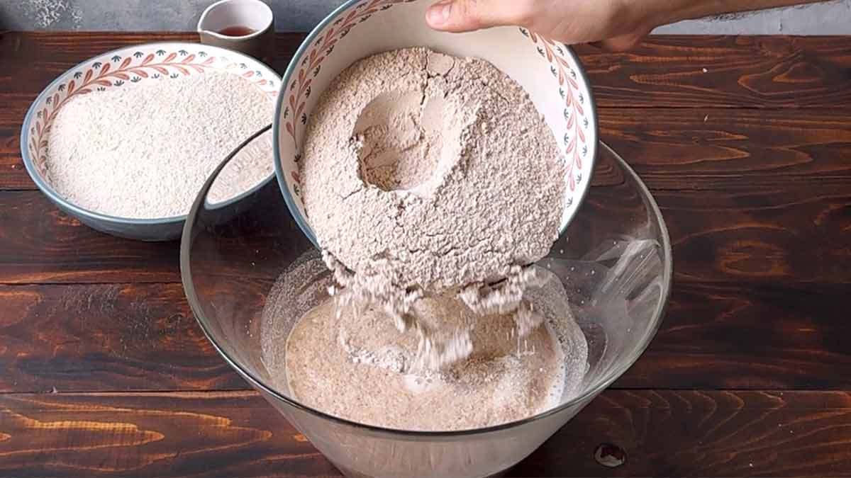 Adding whole barley flour to the bowl with the yeast mixture.
