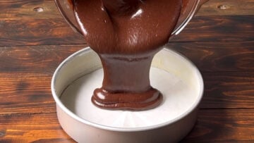 Chocolate cake batter being poured in a round cake pan.