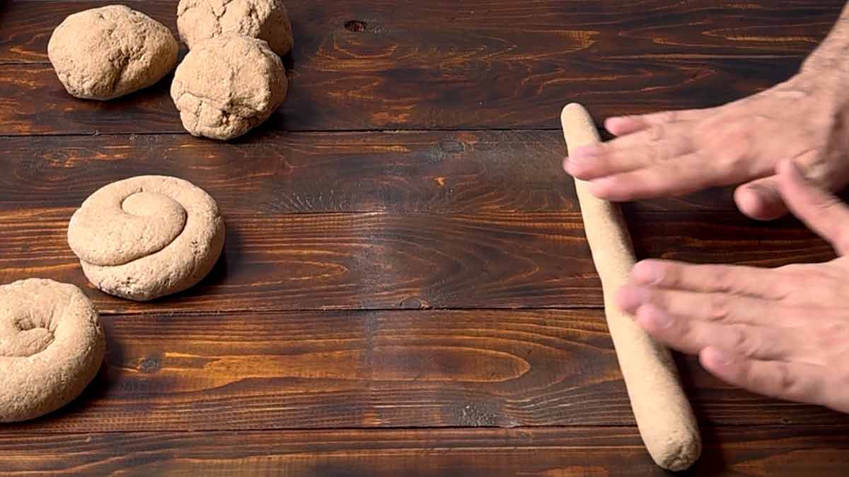 A hand rolling the bread dough into small loaves.