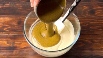 Adding pistachio butter in a bowl with melted white chocolate.
