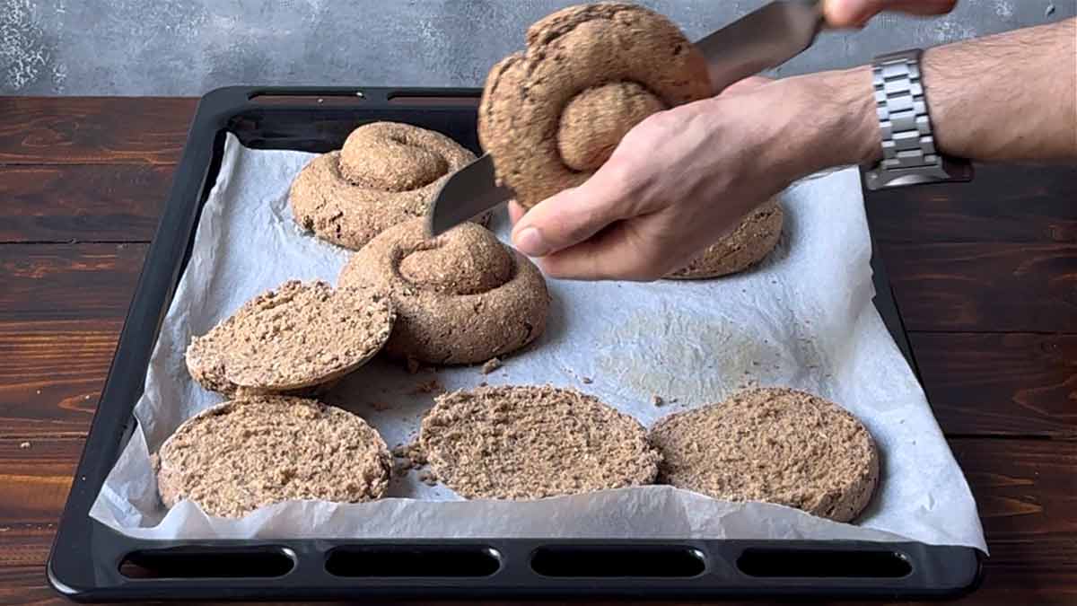 A hand cutting the rusks in the middle with a serrated knife.