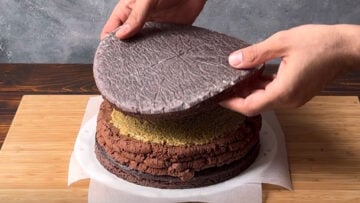 Two hands placing a second cake layer over the pistachio filling.
