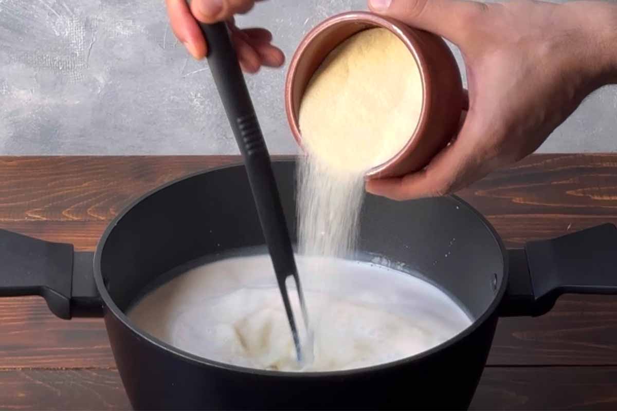 A hand adding semolina to a pot with milk.