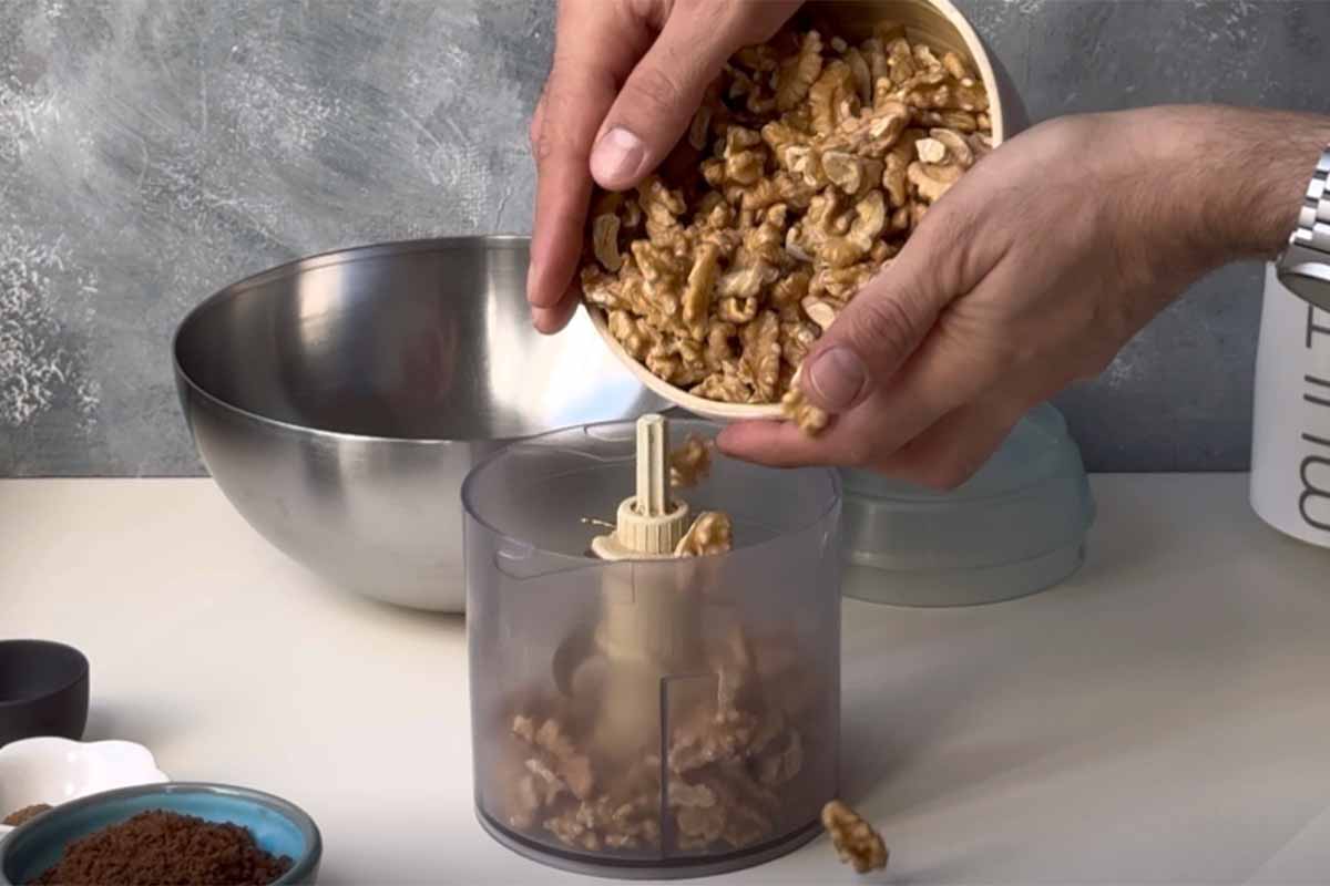 Two hands adding walnuts in a food processor.