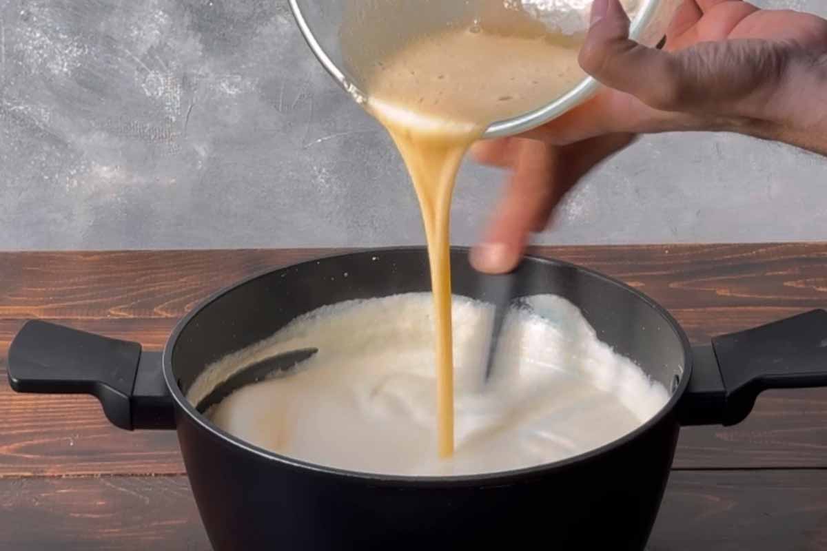 A hand adding beaten eggs to semolina cream.