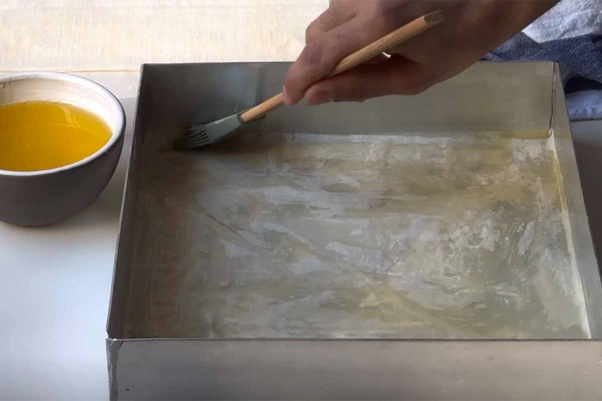 Brushing the phyllo sheets with melted butter in the pan.