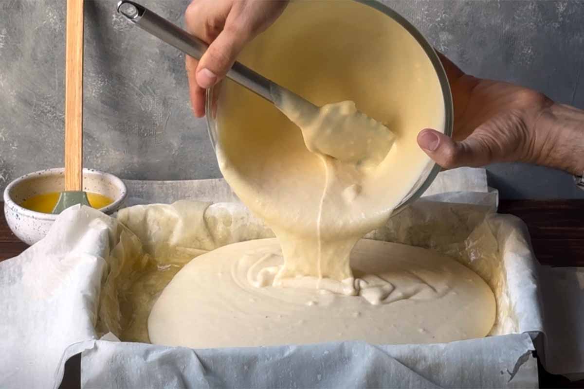 Two hand pour the semolina custard over the phyllo sheets.