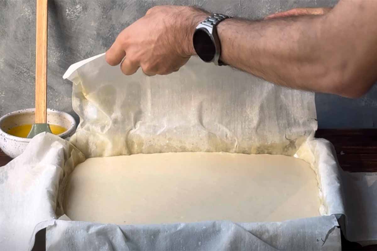 A hand folding the phyllo sheets over the galaktoboureko custard cream.