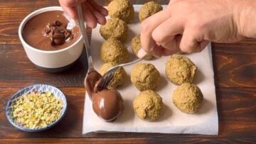 A hand dipping the balls in melted dark chocolate.