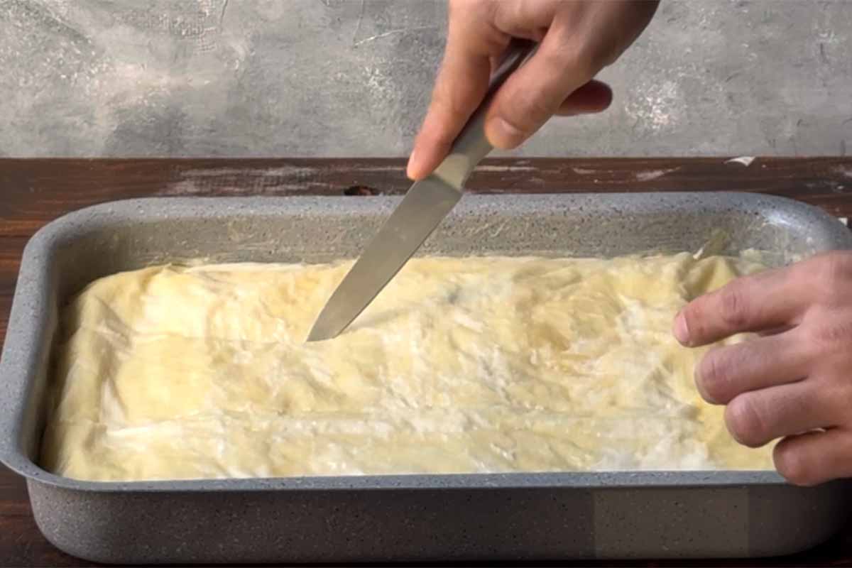 A hand scoring the galaktoboureko with a knife.