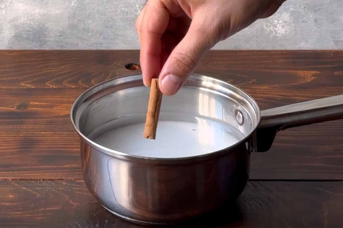 A hand adding a cinnamon stick in a pot with water and sugar.