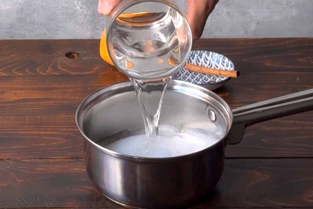A hand adding water in a saucepan with sugar.