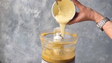 A hand adding melted white chocolate to the pistachio mixture.