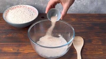 A hand adding active dry yeast to a bowl with water.