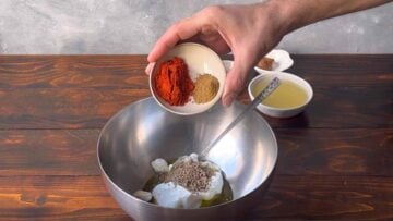 A hand adding spices to a bowl with Greek yogurt.