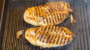 Two chicken breasts cooking on the grill.