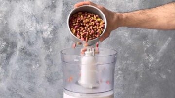 A hand adding roasted pistachio nuts to a food processor.