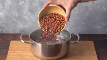 A hand adding pistachios to a pot with boiling water.