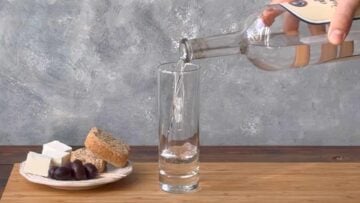 A hand pouring ouzo in a tall narrow glass.