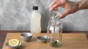 A hand pouring ouzo liquor in a glass jar.