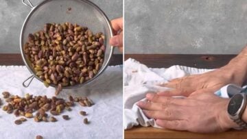A hand peeling the skins of the pistachio nuts.
