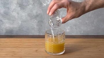 A hand pouring ouzo into a glass.