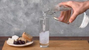 A hand pouring water over ouzo.