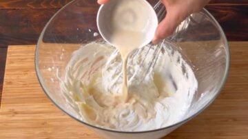 A hand adding milk to the butte rmixture.