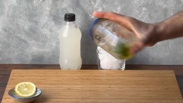 A hand shaking a jar with ouzo, lemon juice, honey and spearmint leaves.
