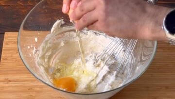 A hand cracking an egg over the butter and sugar mixture.