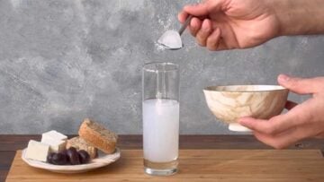 A hand adding ice cubes to the glass.