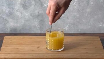 A hand stirring the cocktail with a spoon.