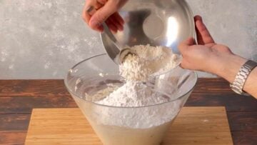 Two hands adding flour to the bowl.