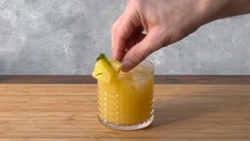 A handing adding a piece of pineapple on the rim of the glass.