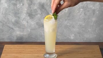 A hand adding a sprig of spearmint to the drink.