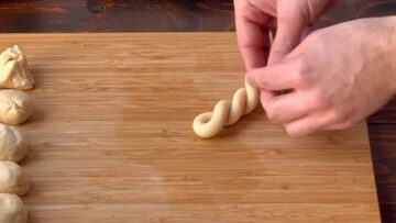 Two hands twisting a long piece of cookie dough.