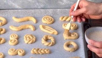 A hand brushing the cookies with egg wash.