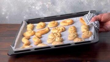 A hand holding a baking sheet with baked Greek butter cookies.
