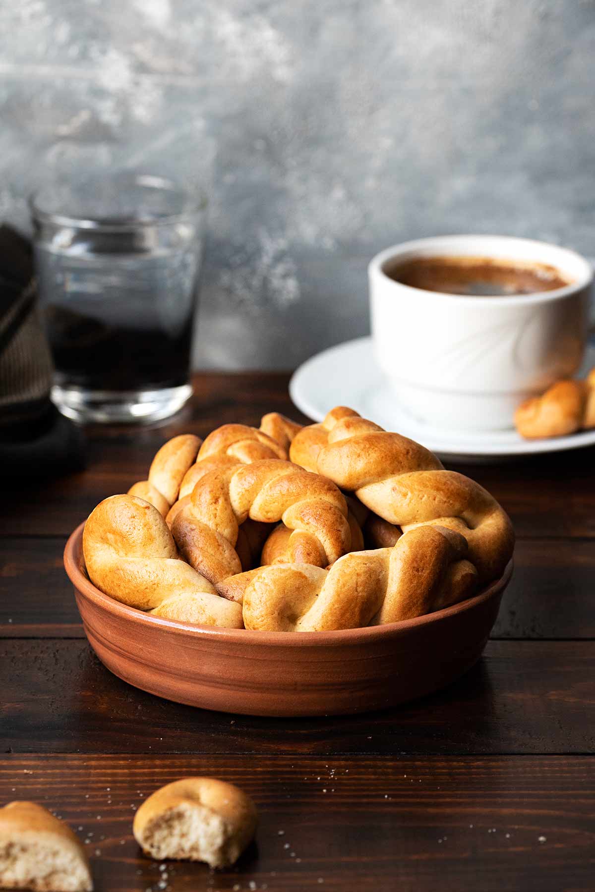 A clay bowl with Greek Easter cookies, a cup of coffee and a glass of water.