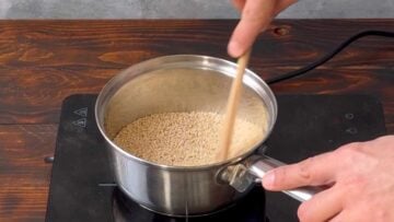 A hand stirring sesame seeds in a pot with a spatula.