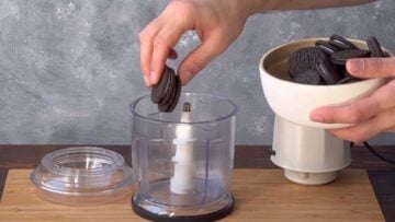 A hand transferring Oreo cookies into a food processor.