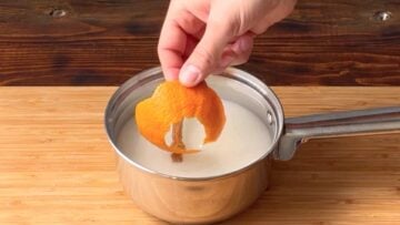 A hand adding orange peel to a saucepan with sugar and water.