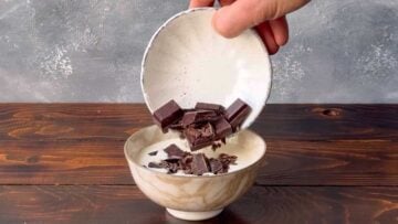 A hand adding chopped dark chocolate to a bowl with heavy cream.