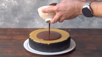 A hand pouring the chocolate topping over the pistachio cheesecake.