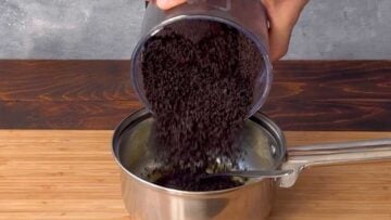 A hand adding cookie crumbs into a pot with melted butter.