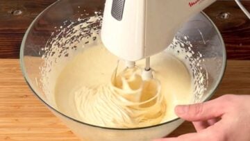 A hand mixer whipping eggs in a bowl.