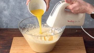 A hand adding melted butter to the whipped eggs.