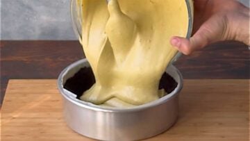 A hand pouring the pistachio filling over the crust.