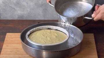 Two hands adding hot water to a large pan with a smaller pan inside.