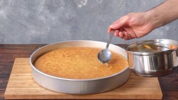 A hand pouring syrup over the revani.